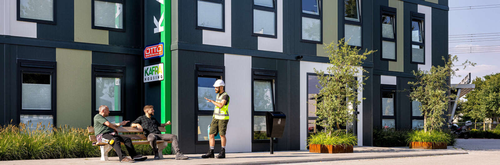 Unterhaltung dreier Arbeiter vor einem Wohnhaus.