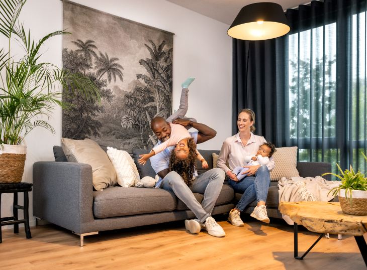 Zwei Eltern mit zwei Kindern lächeln und spielen im Wohnzimmer ihres Modulhauses im Erdgeschoss